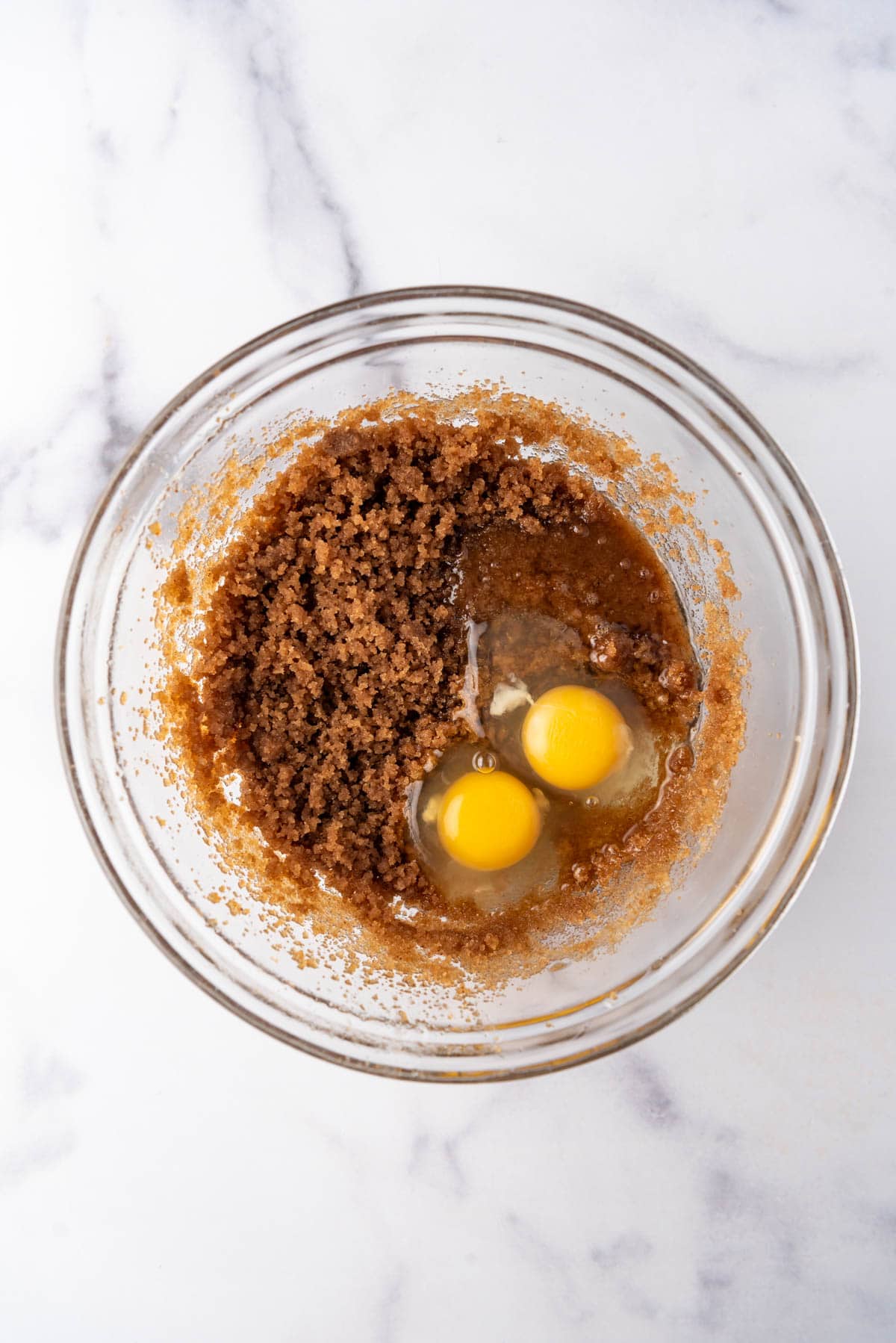 Adding eggs to browned butter and sugar in a large glass bowl.