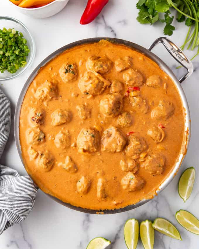 An overhead image of a pan of chicken meatballs in creamy coconut curry sauce surrounded by fresh vegetables.