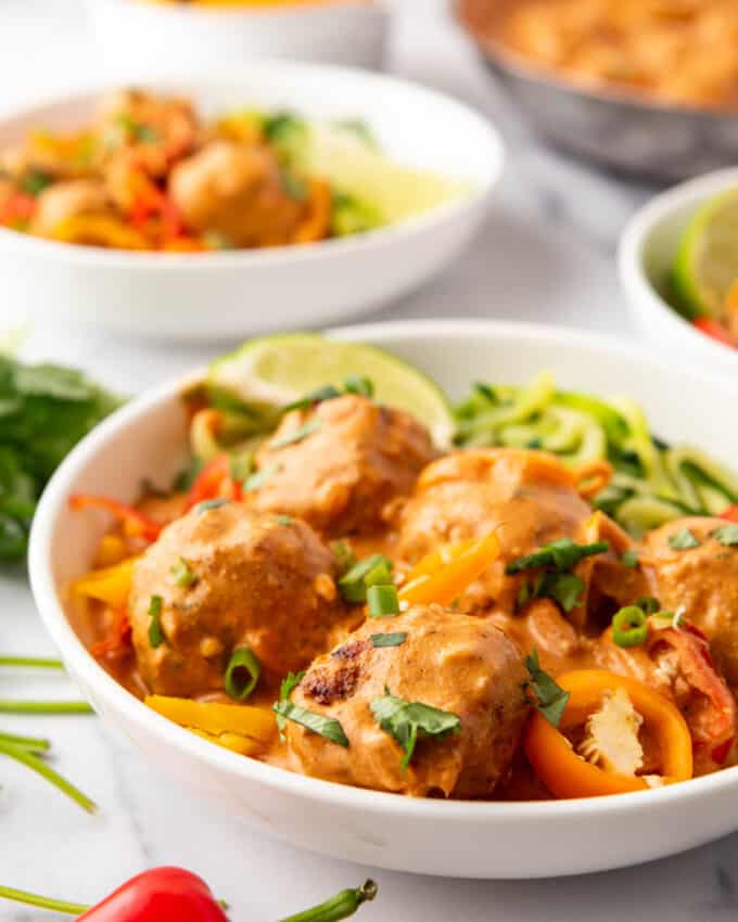 White pasta bowls of zoodles with coconut curry chicken meatballs.