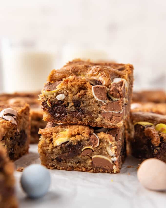 Blondies cut into squares and stacked with Cadbury mini eggs scattered around them.