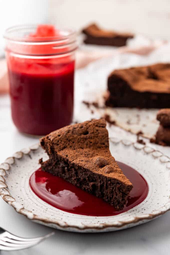 An image of a slice of flourless chocolate cake on a plate with raspberry sauce.