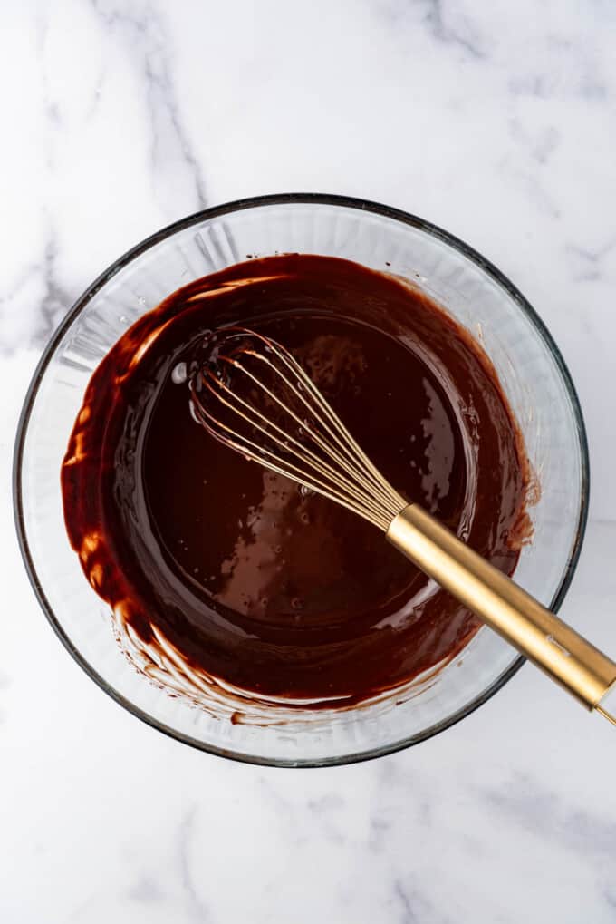 Melted chocolate and butter in a glass bowl with a whisk.