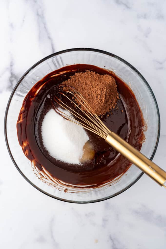 Adding granulated sugar, cocoa powder, and vanilla extract to a glass mixing bowl.