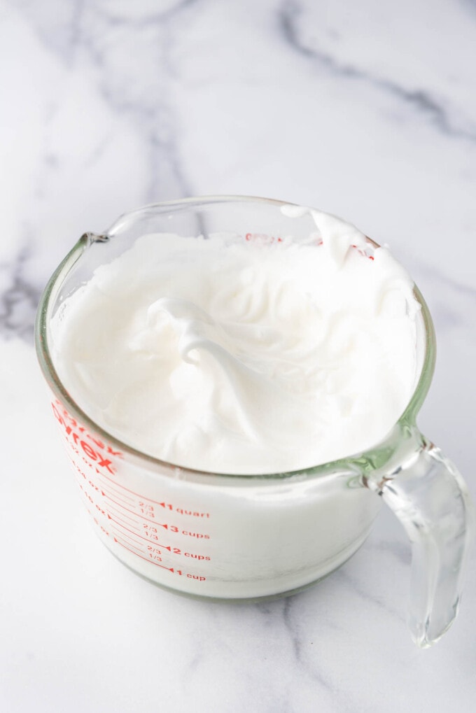 Egg whites and sugar whipped into stiff peaks in a glass mixing bowl.