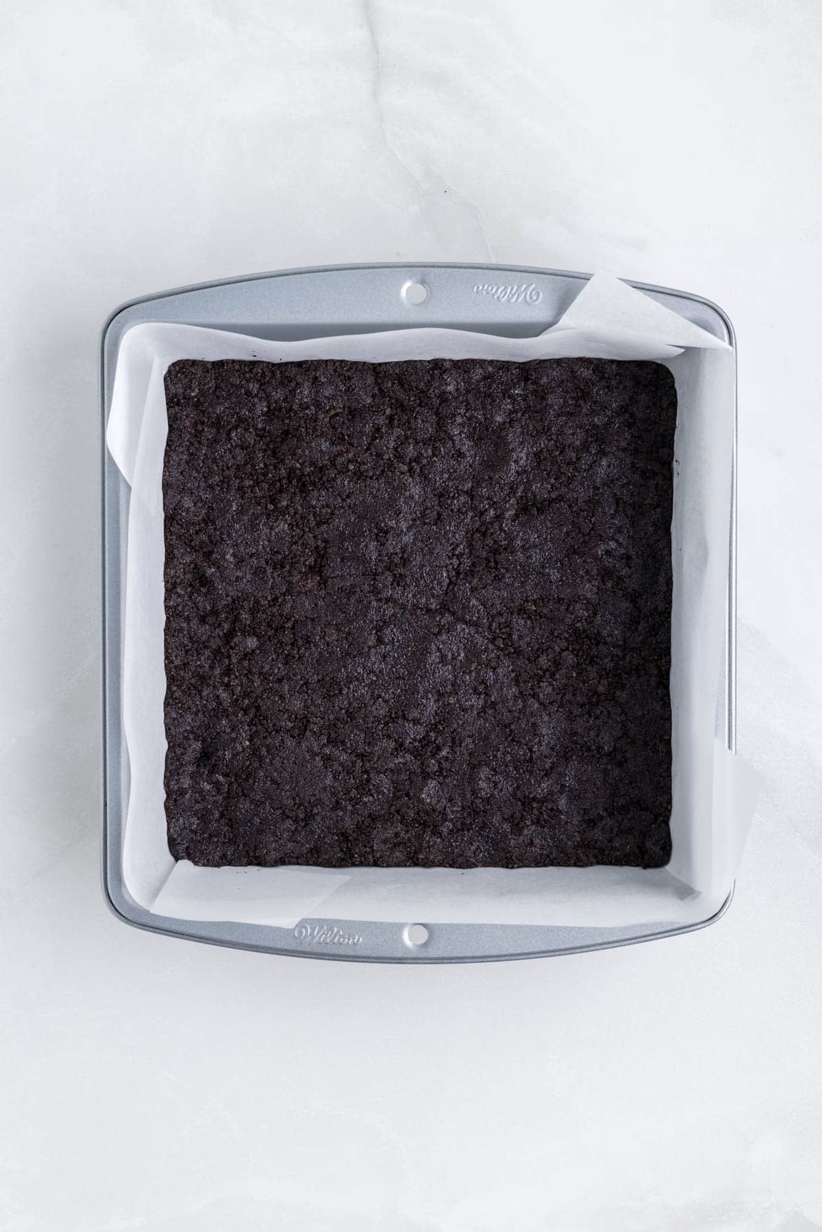 Oreo cookie crust in a square pan lined with parchment paper.