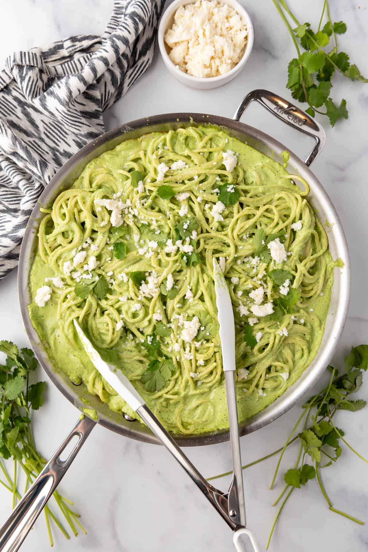 An overhead image of a large skillet full of spaghetti verde with tongs in it for serving.