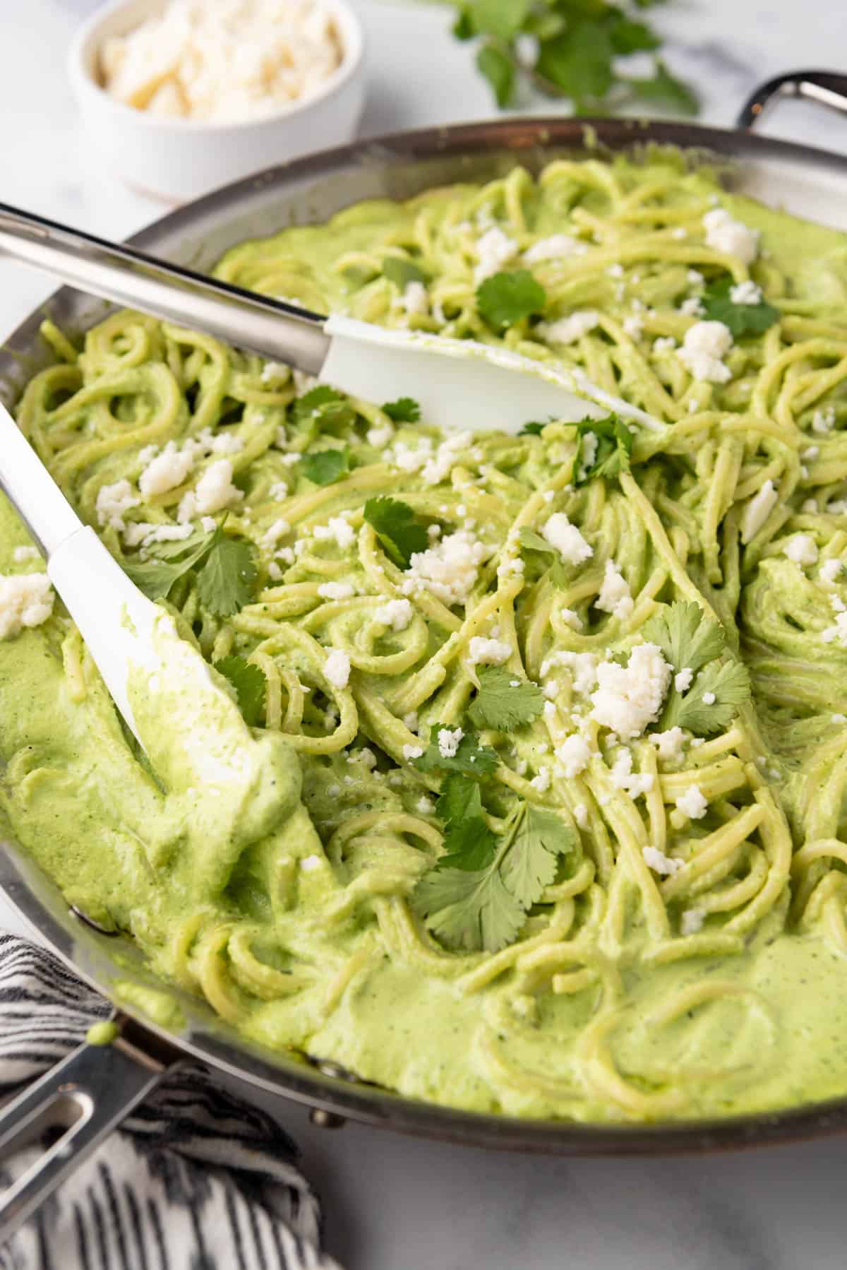 Spaghetti verde in a pan with cilantro and queso fresco sprinkled on top.