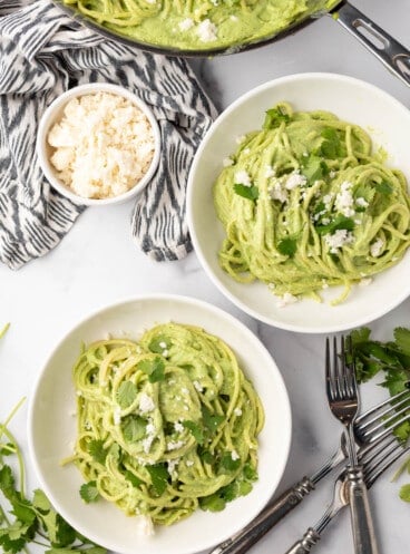 Two white pasta bowls full of spaghetti verde.