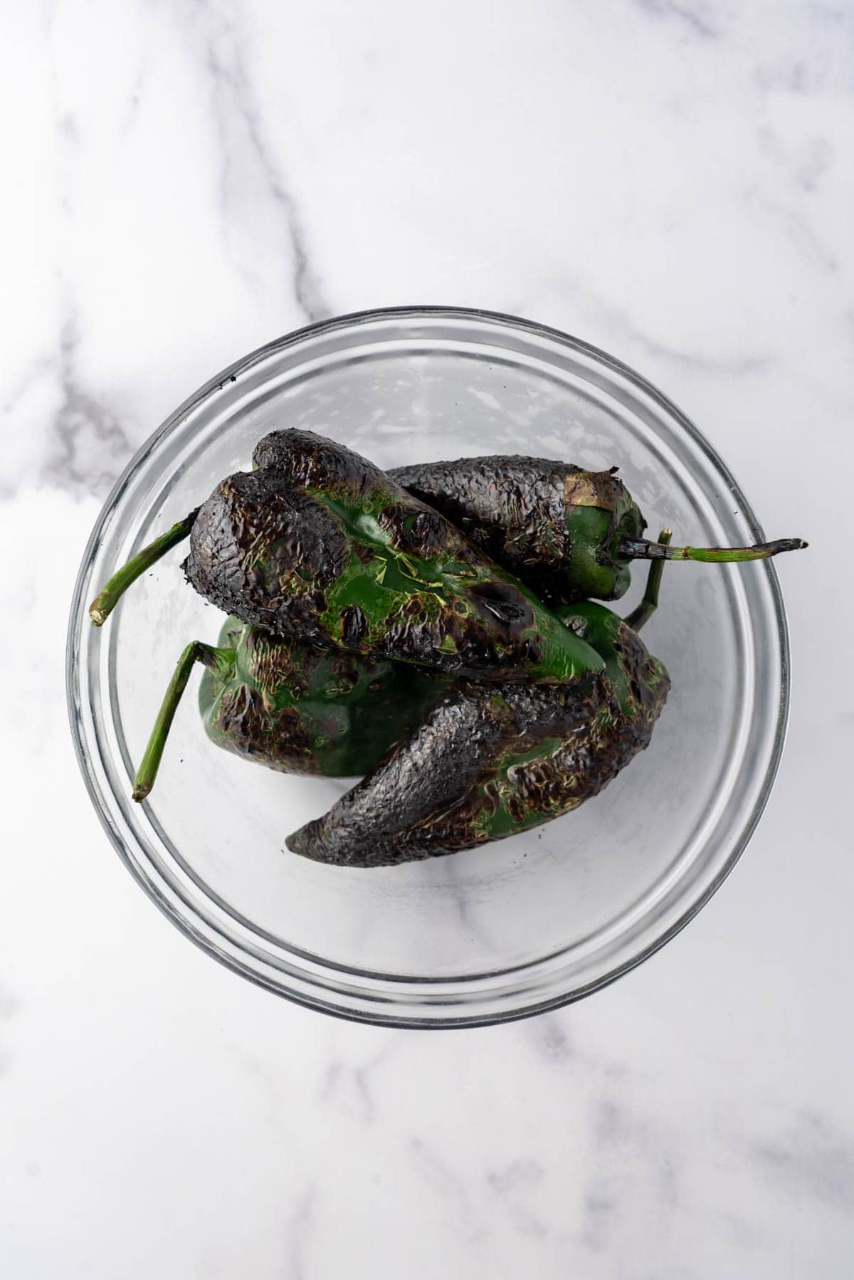 Charred poblano peppers in a glass bowl.