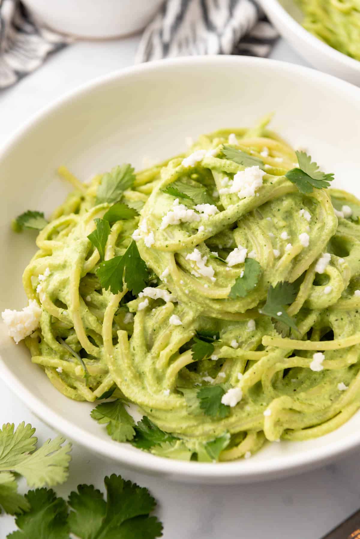 A close image of a bowl of spaghetti verde with fresh cilantro leaves and crumbled queso fresco on top.