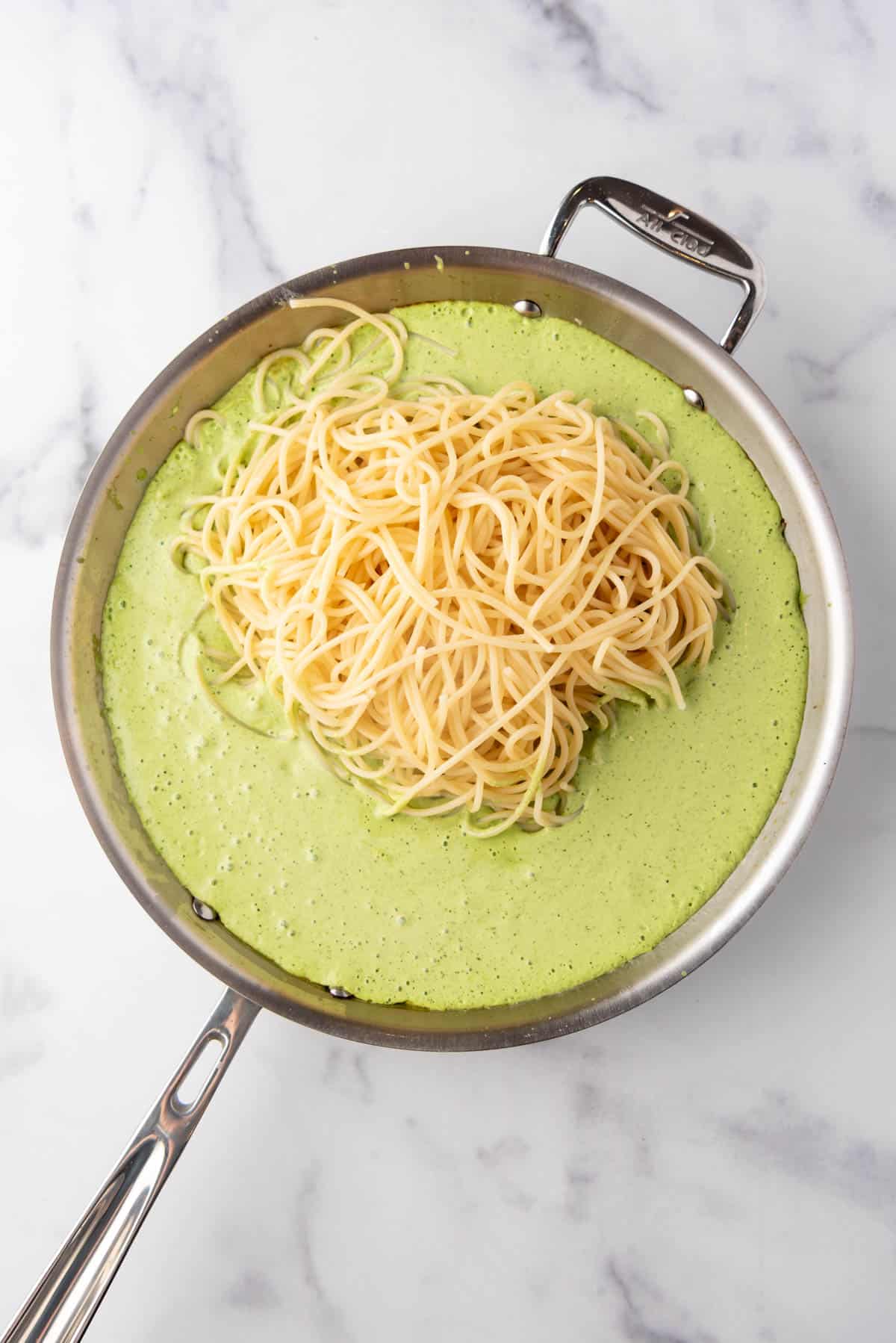 Adding cooked pasta to creamy poblano sauce in a large skillet.