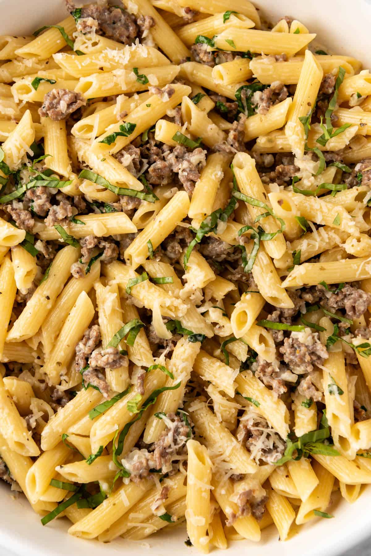 A close image of cooked Italian sausage and basil with penne pasta in a creamy garlic sauce.