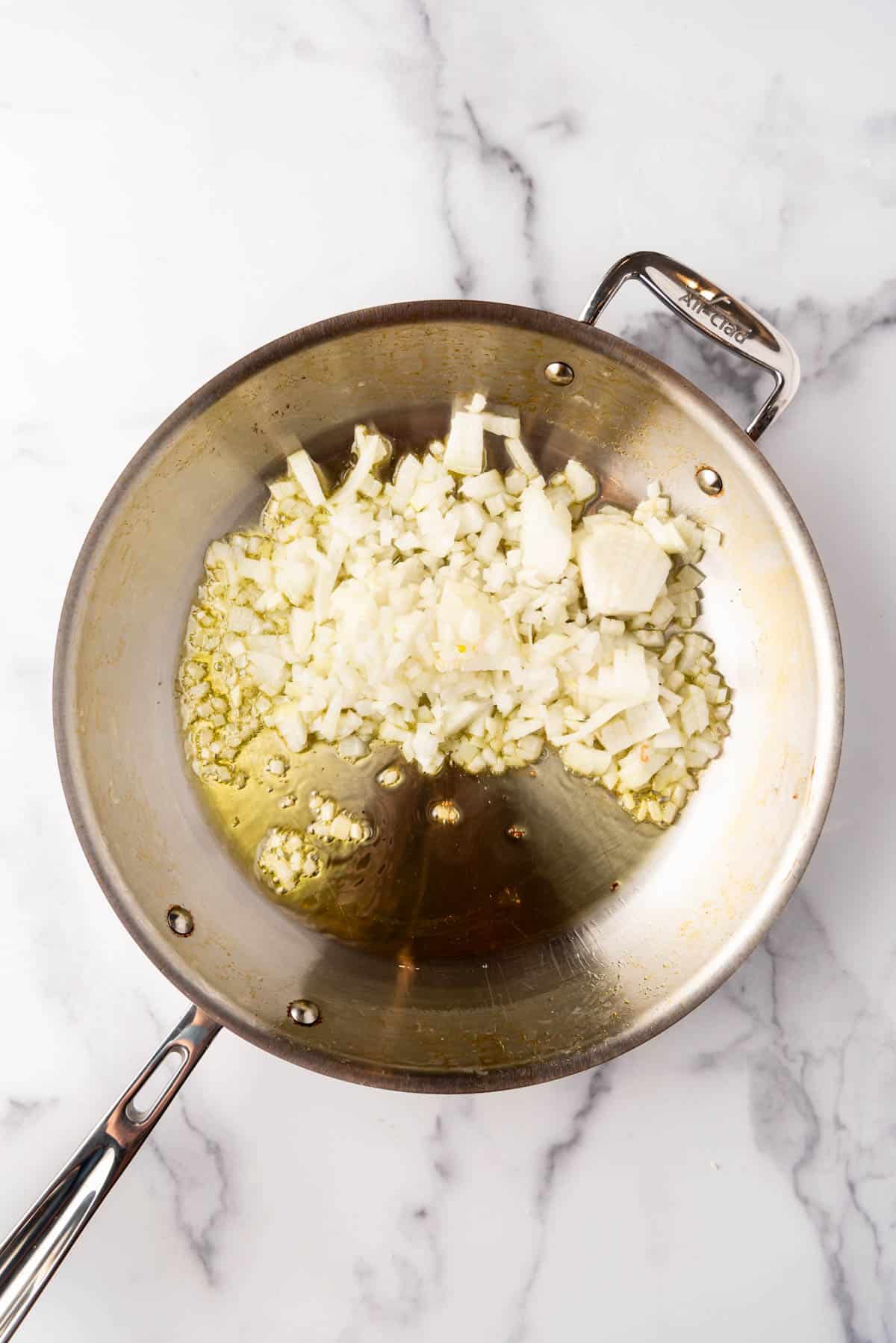 Sauteeing chopped onions and garlic in olive oil in a large skillet.