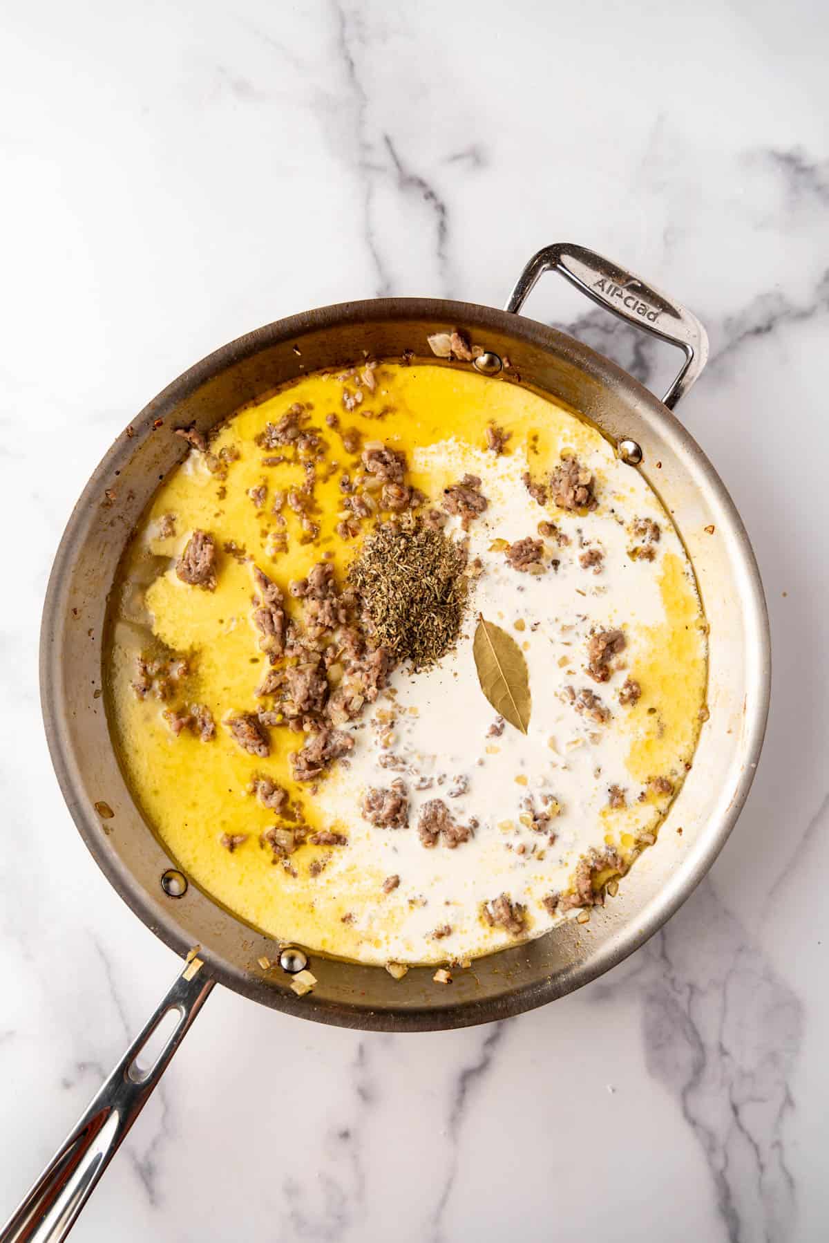 Adding heavy cream to a large pan of browned Italian sausage.