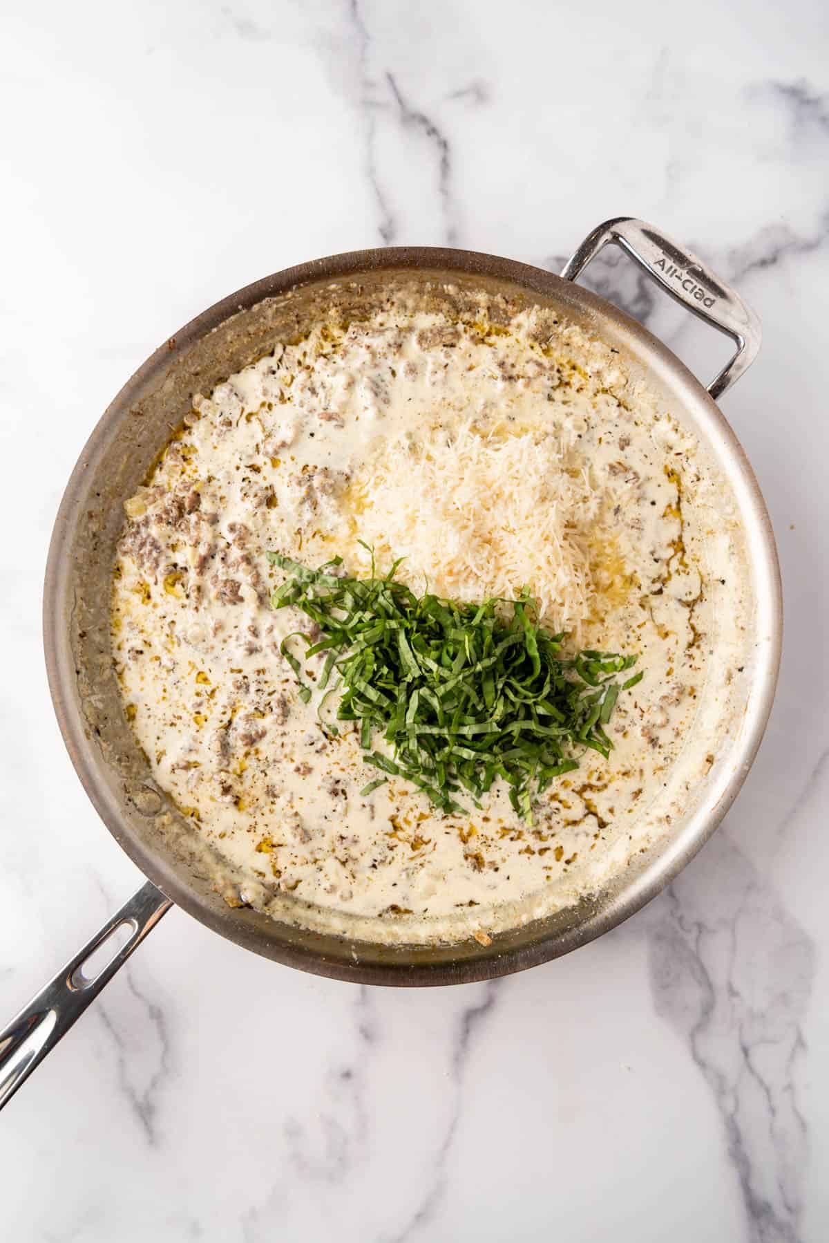 Adding thinly sliced fresh basil and grated parmesan cheese to a cream sauce in a large skillet.