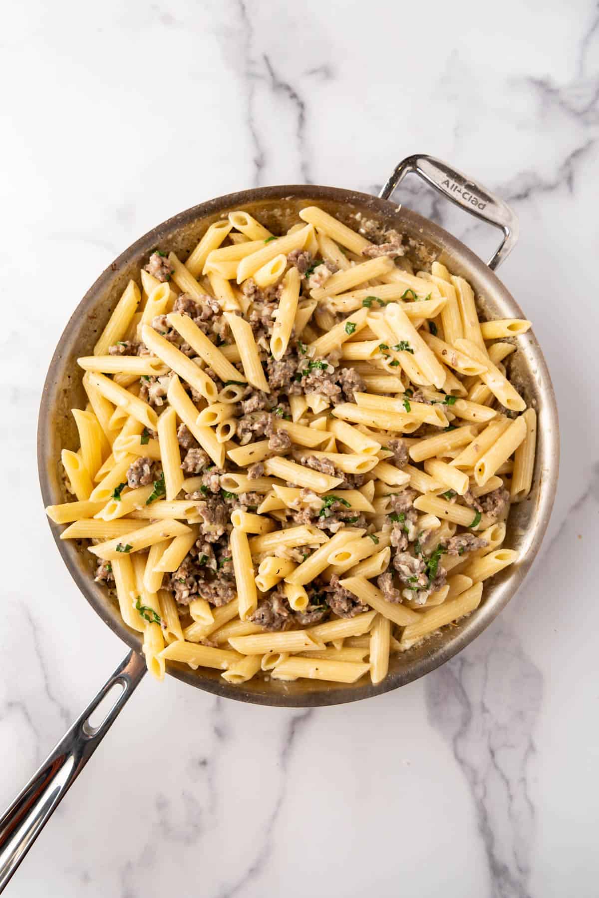 An overhead image of a finished recipe of penne pasta with Italian sausage in a garlic cream sauce.