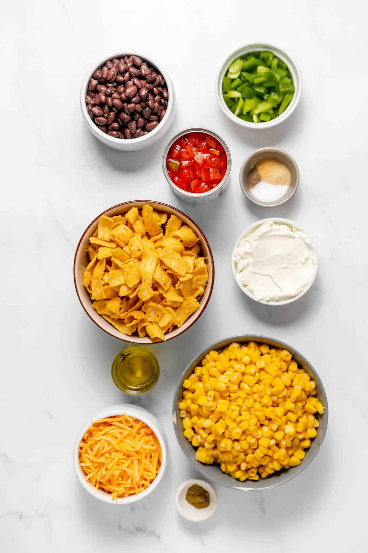 Ingredients for Frito corn salad in separate bowls on a white surface.