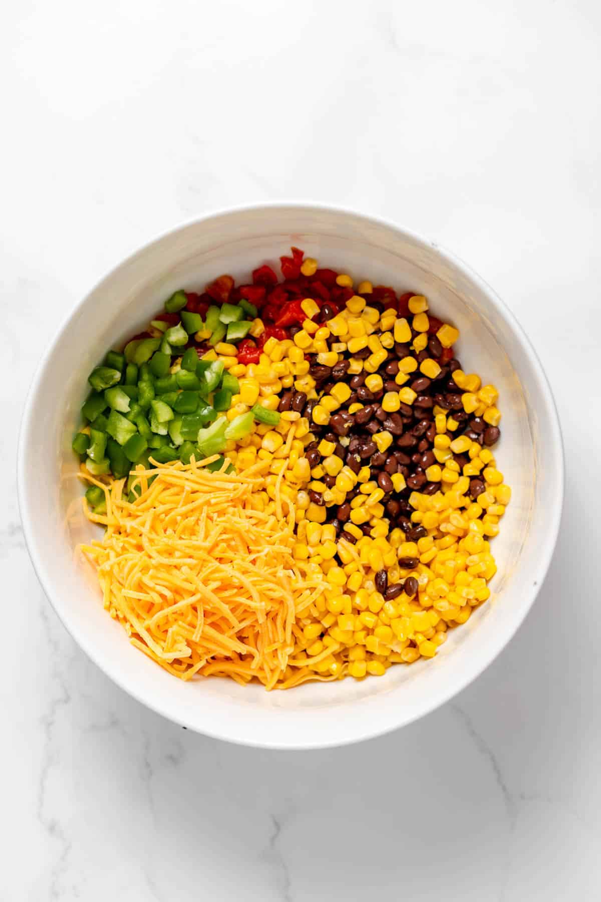 A bowl full of corn, black beans, chopped peppers, and shredded cheddar cheese.