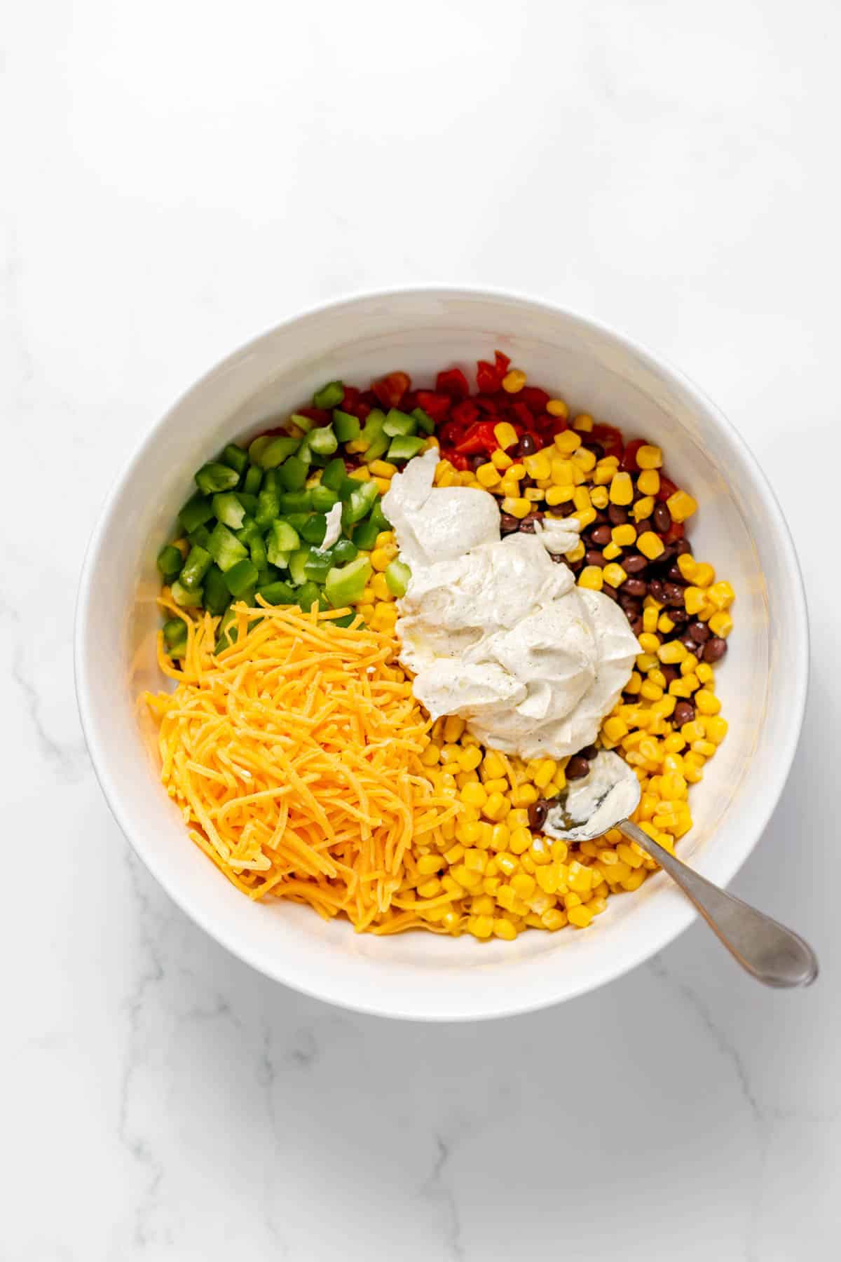 Adding creamy dressing to a bowl of Frito corn salad ingredients.