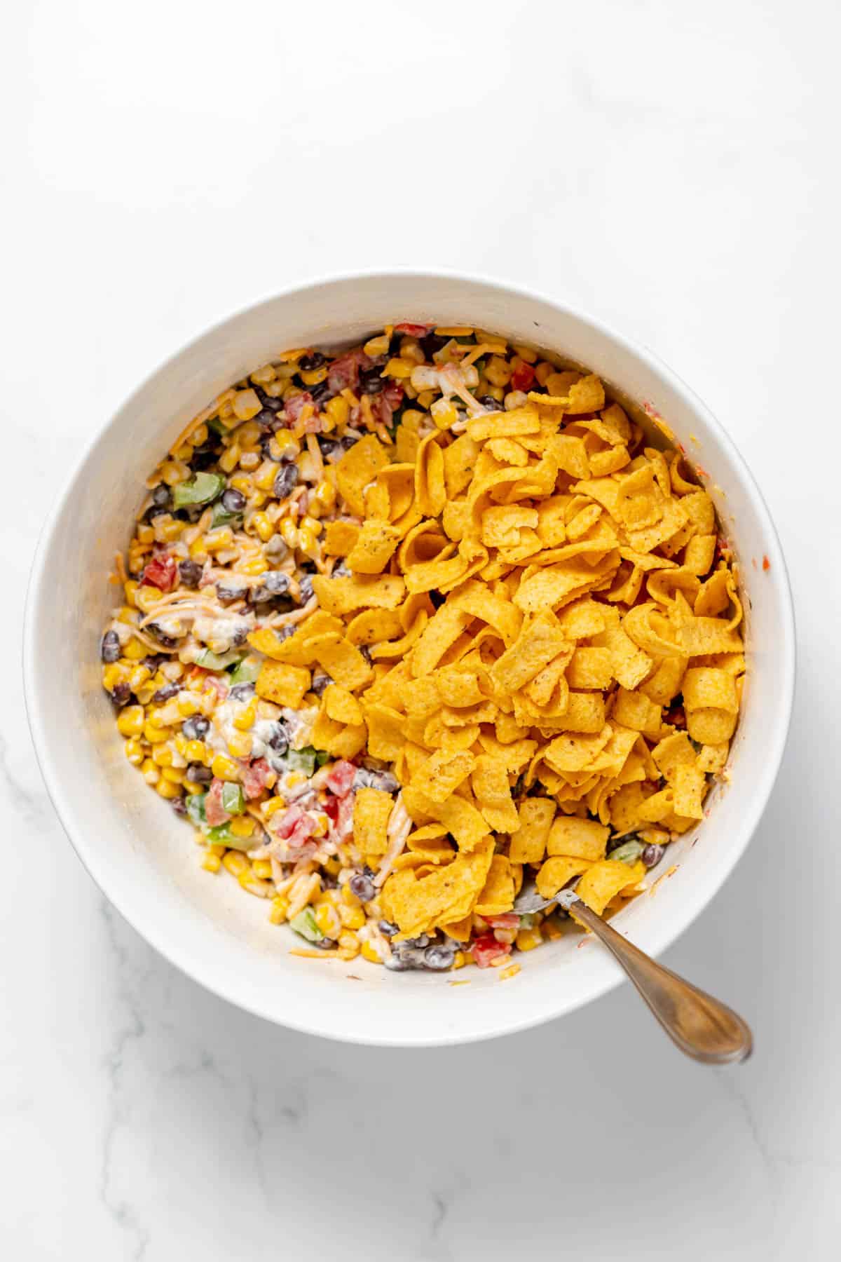 Adding Frito corn chips to a bowl of salad ingredients.