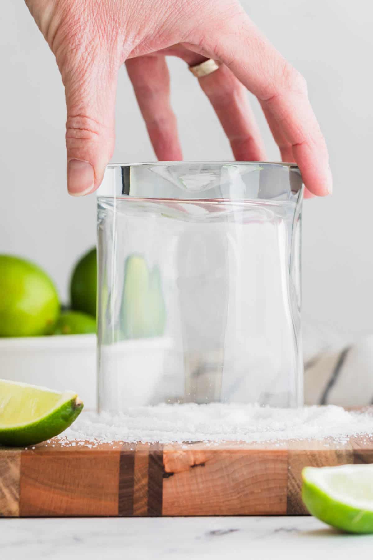 A hand twisting a glass in coarse salt to coat the rim.