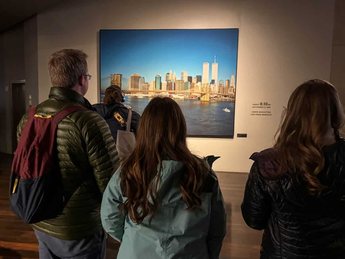 A dad and two daughters in the 9/11 memorial museum looking at an image of the New York City skyline on the morning of 9/11.