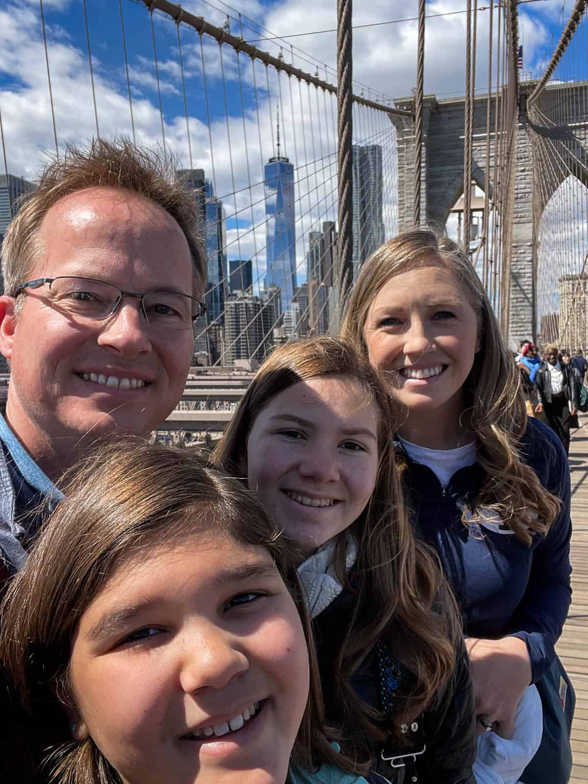 A family of four taking a selfie on the Brooklyn Bridge.