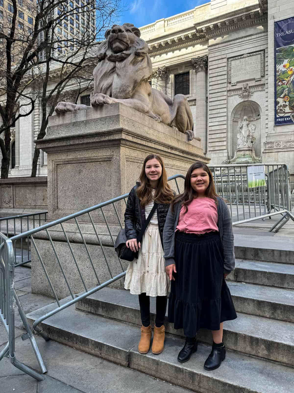Two girls in front of one of the New York City Public Library lion statutes.