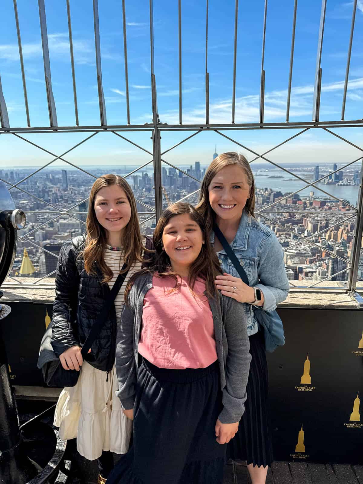A mom and two daughters on the top of the Empire State Building in NYC.