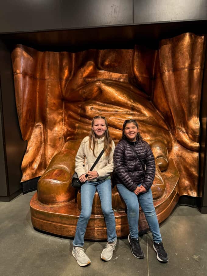 An image of two girls sitting on a replica of the Statue of Liberty's foot.