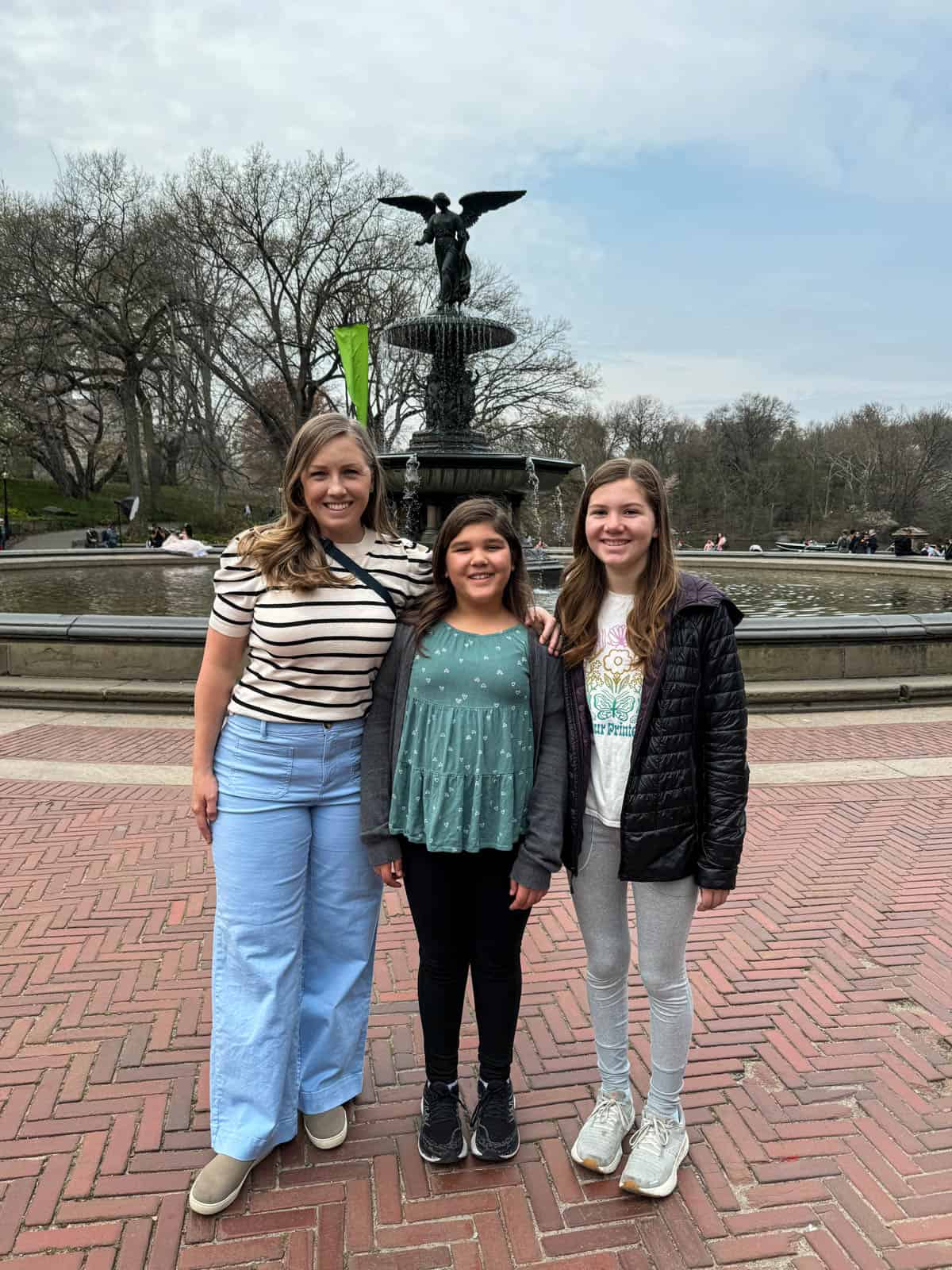 A mom and two daughters in Central Park in front of Bethesda Fountain.