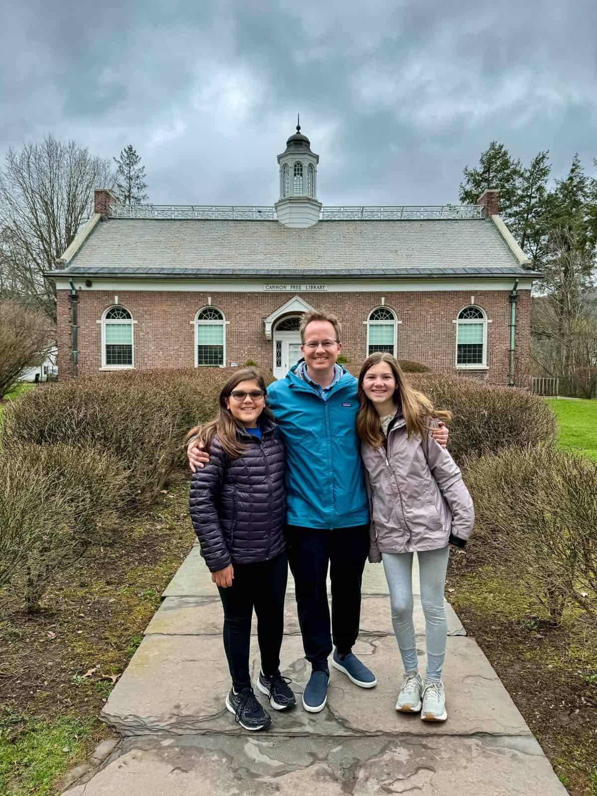 A dad and two daughters in front of the Cannon Free Library from the book "My Side of the Mountain" in upstate New York.