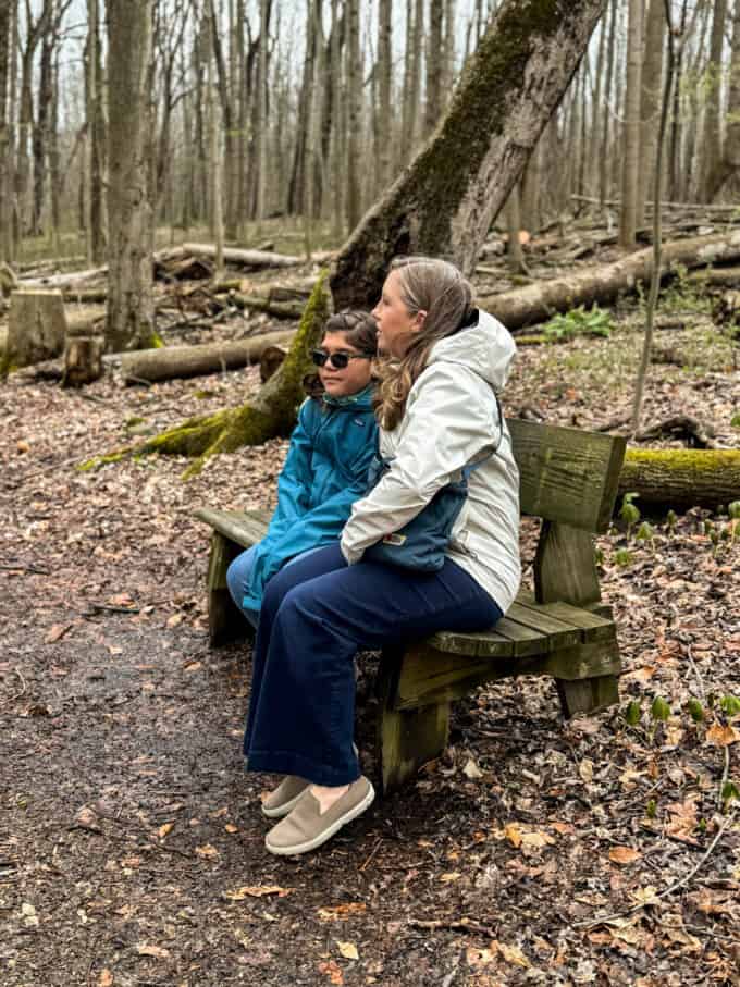 A mom and daughter on a bench in the Sacred Grove.