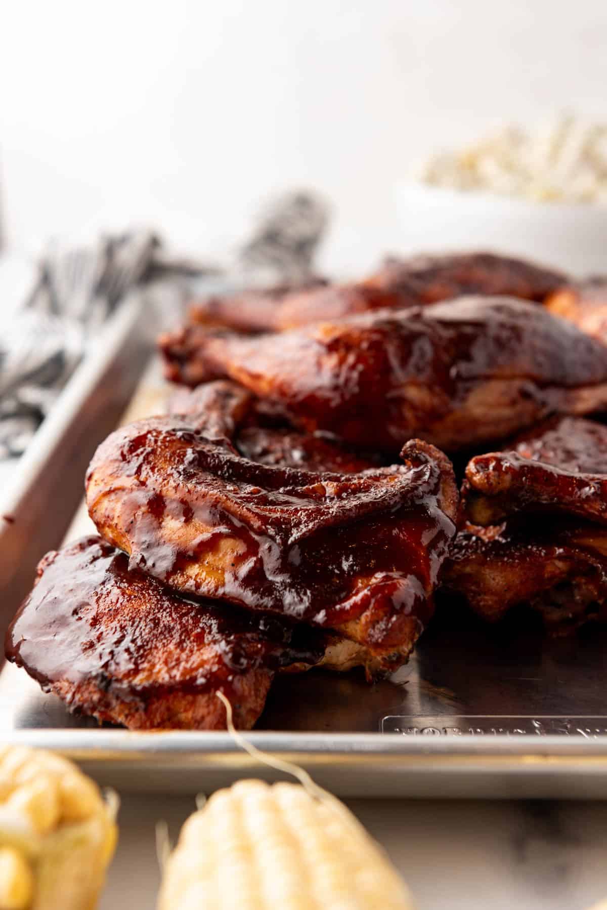 A side angle of smoked chicken quarters on a baking sheet.