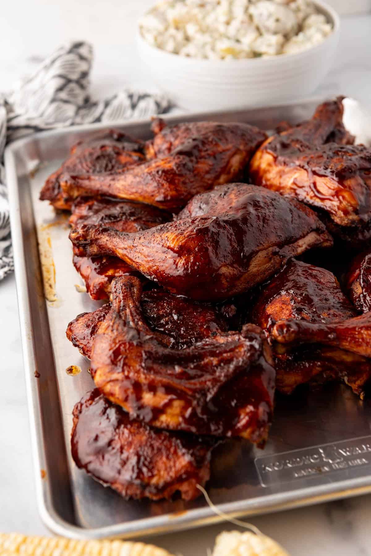 A pan of smoked chicken thighs and quarters with barbecue sauce on them.