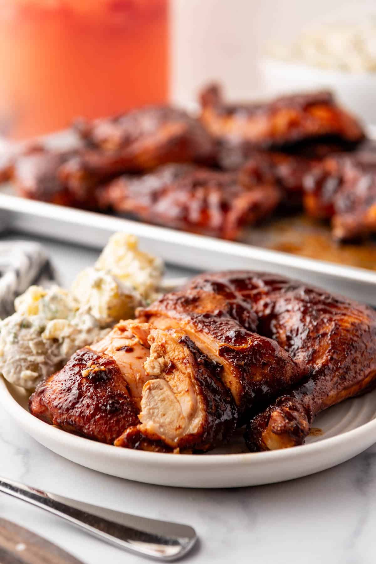 A piece of smoked chicken on a white plate with potato salad.