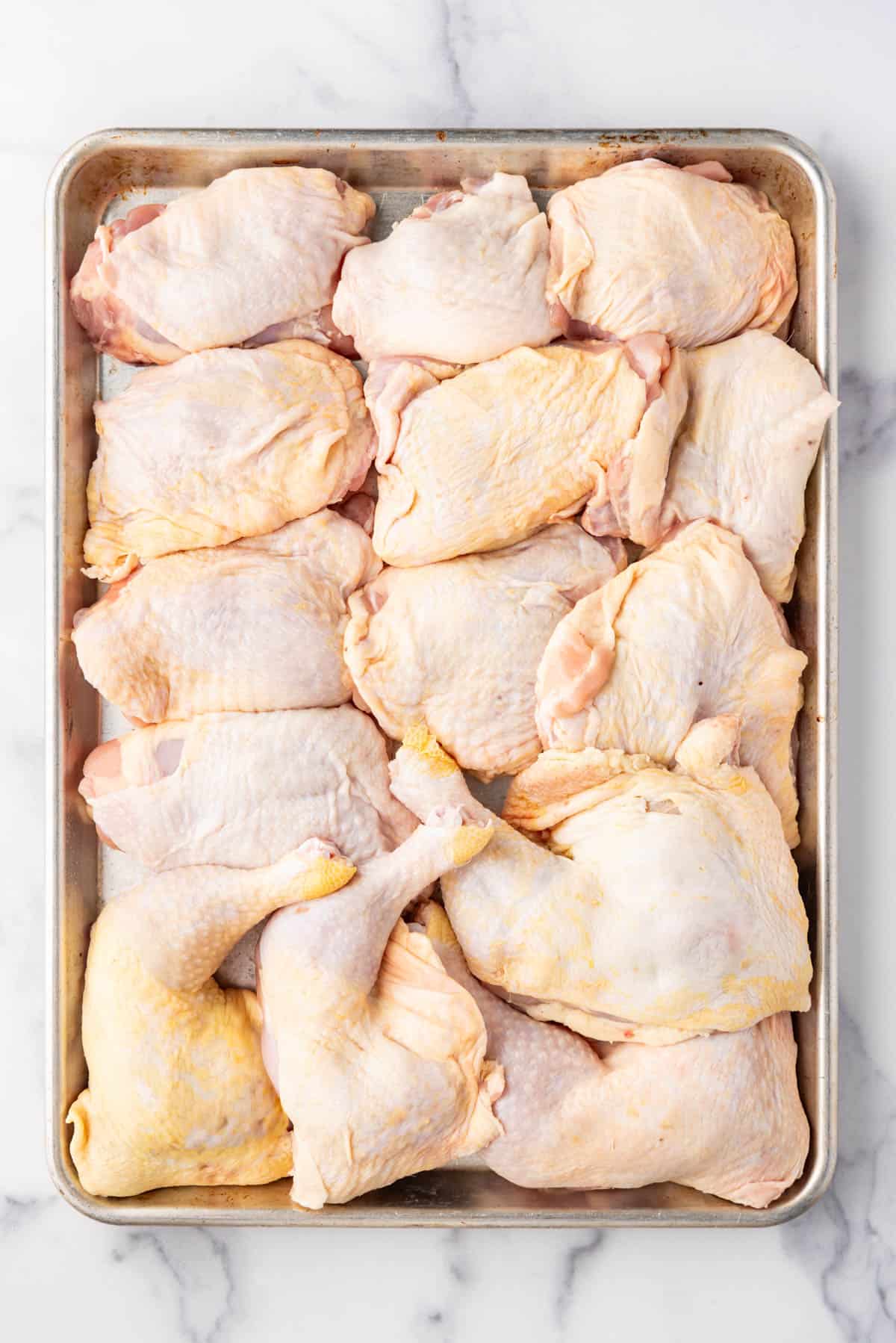 Bone-in chicken pieces on a baking sheet.