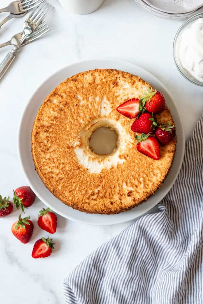 An overhead image of a light and fluffy angel food cake on a white plate decorated with halved strawberries.