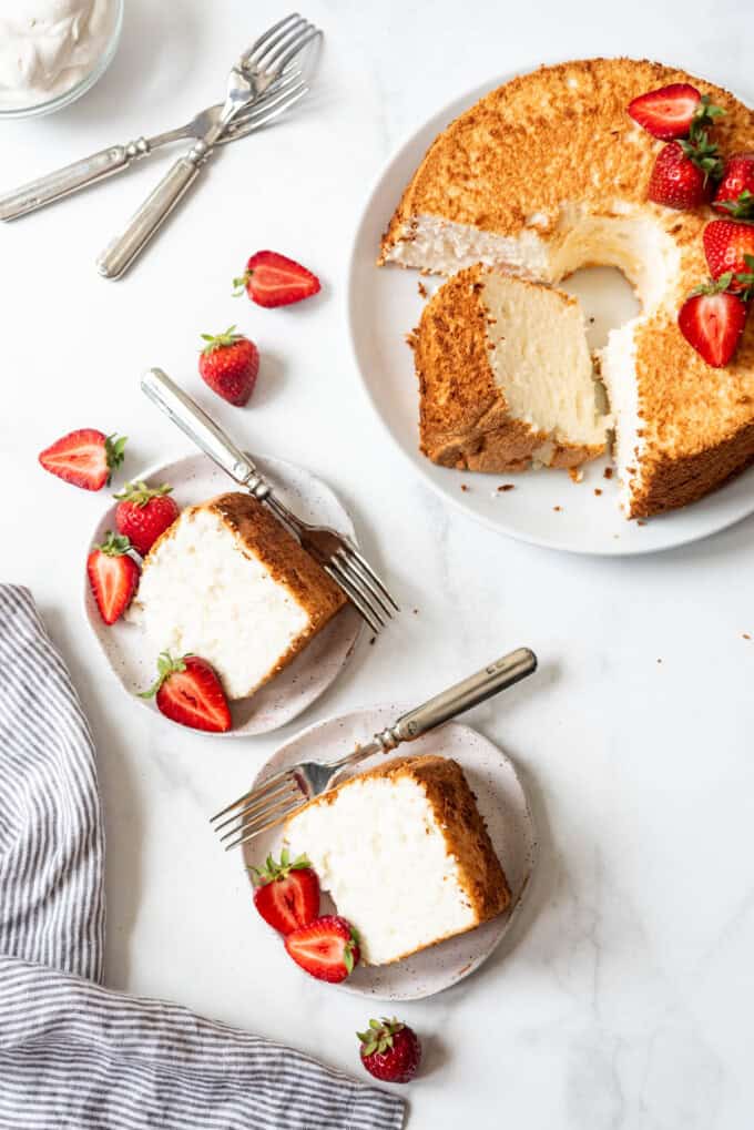 An overhead image of slices of angel food cake on plates with forks next to the rest of the cake.