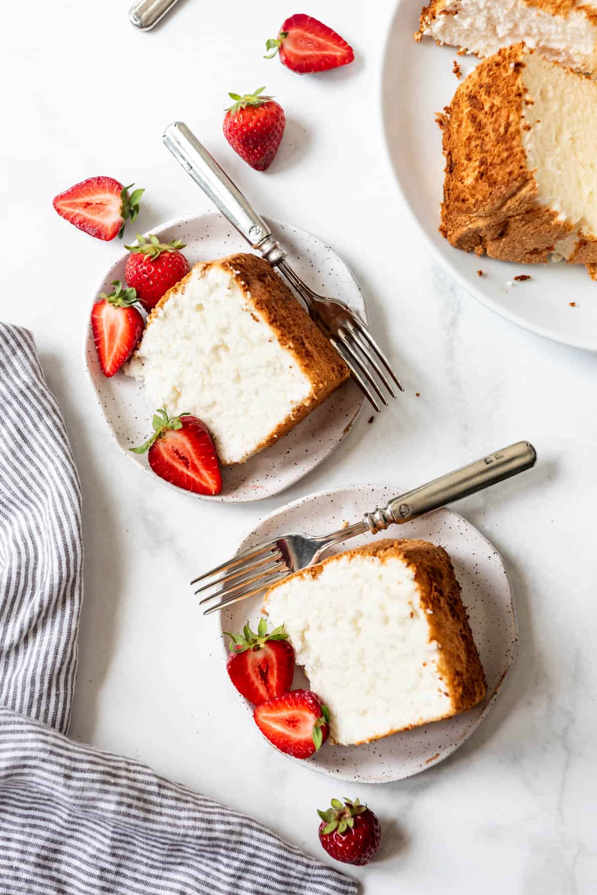 An overhead image of two slices of angel food cake on plates with strawberries.