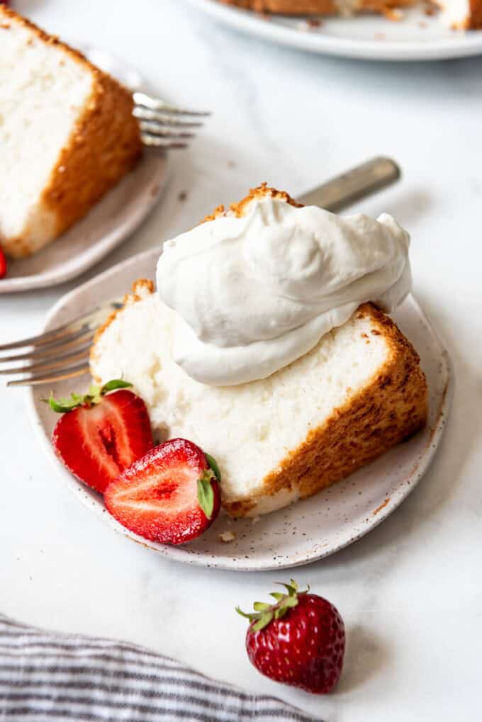 A slice of angel food cake on a plate with whipped cream and strawberries.