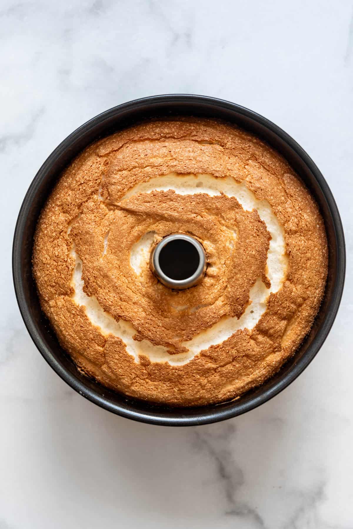 An overhead image of a baked angel food cake in a tube pan.