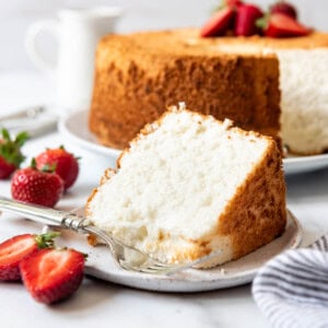 A slice of angel food cake on a plate with a fork and halved strawberries nearby.