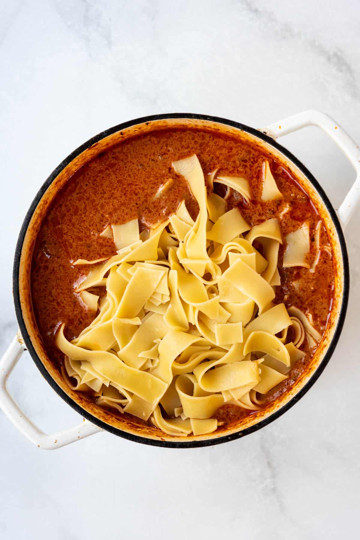 Adding cooked pappardelle pasta to a pot of beef ragu.