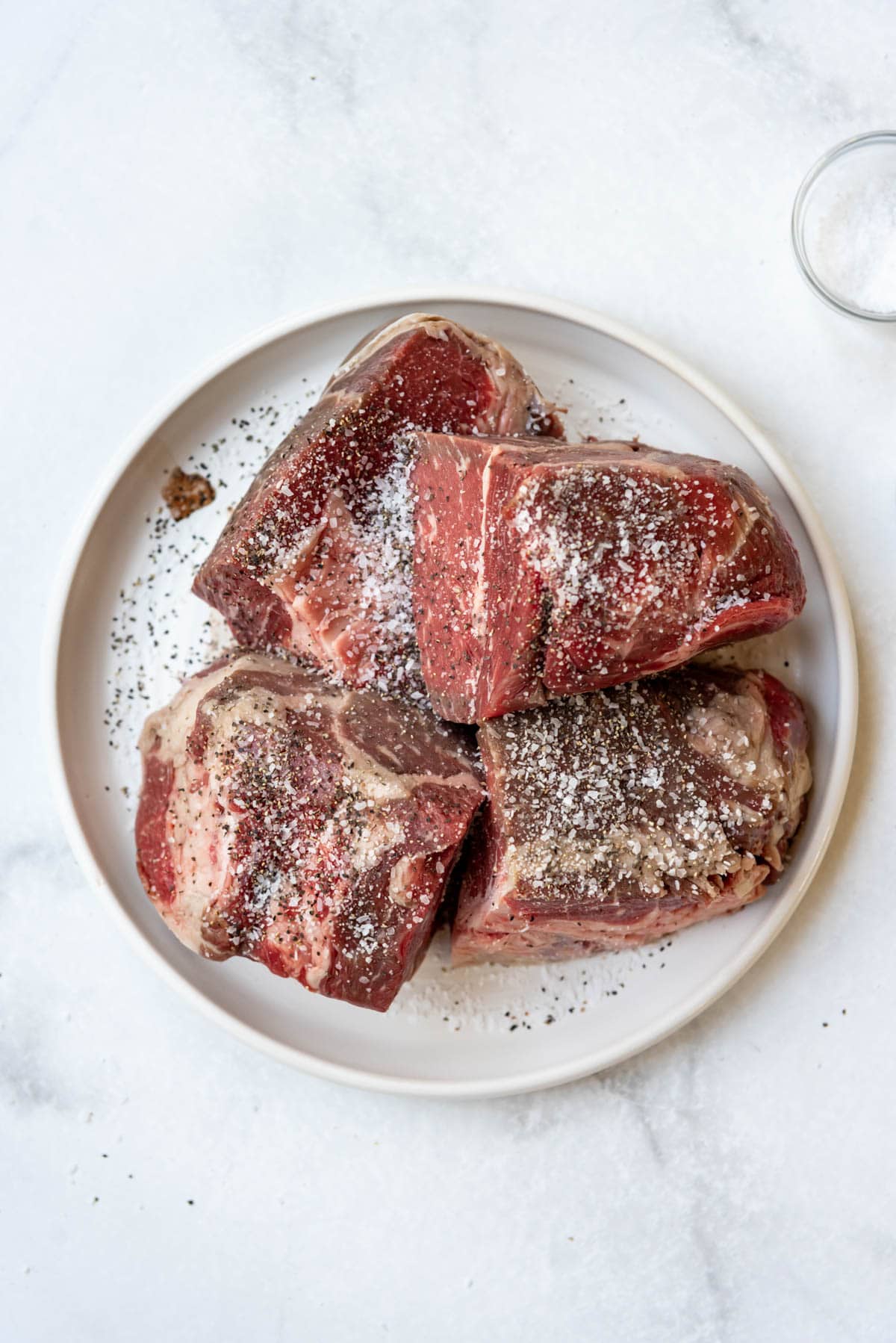 Seasoning chuck roast chunks with kosher salt and freshly ground black pepper.