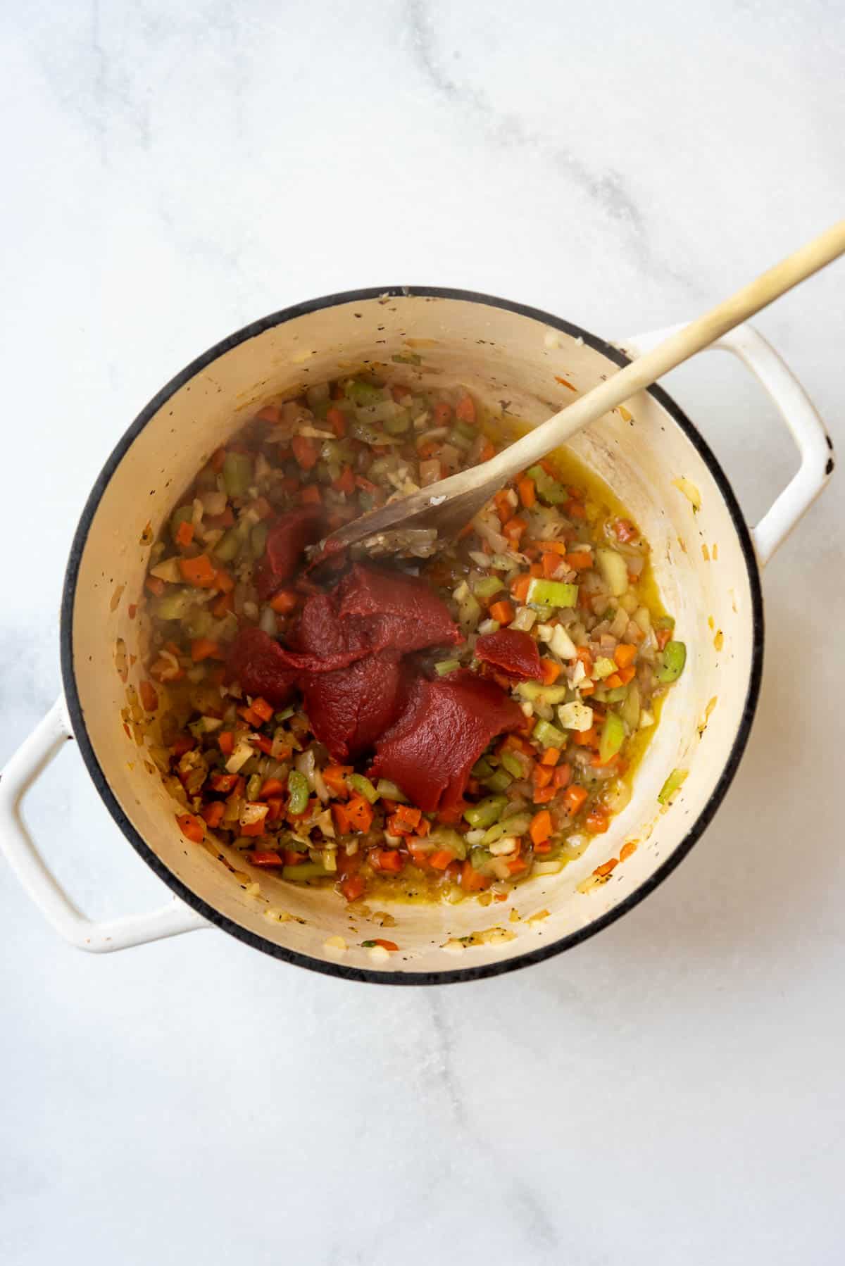 Adding tomato paste to sauteed vegetables.