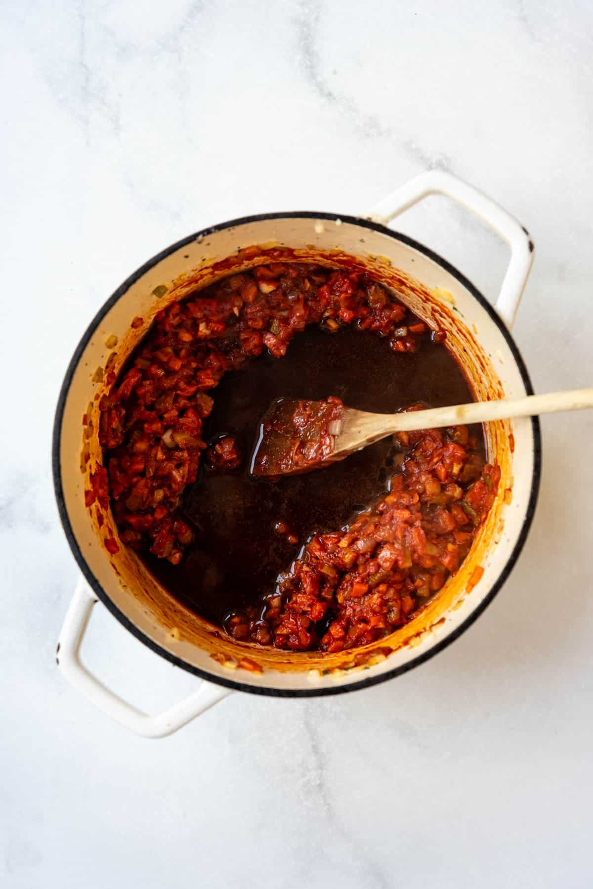 Adding red wine to sauteed vegetables and tomato paste in a dutch oven.