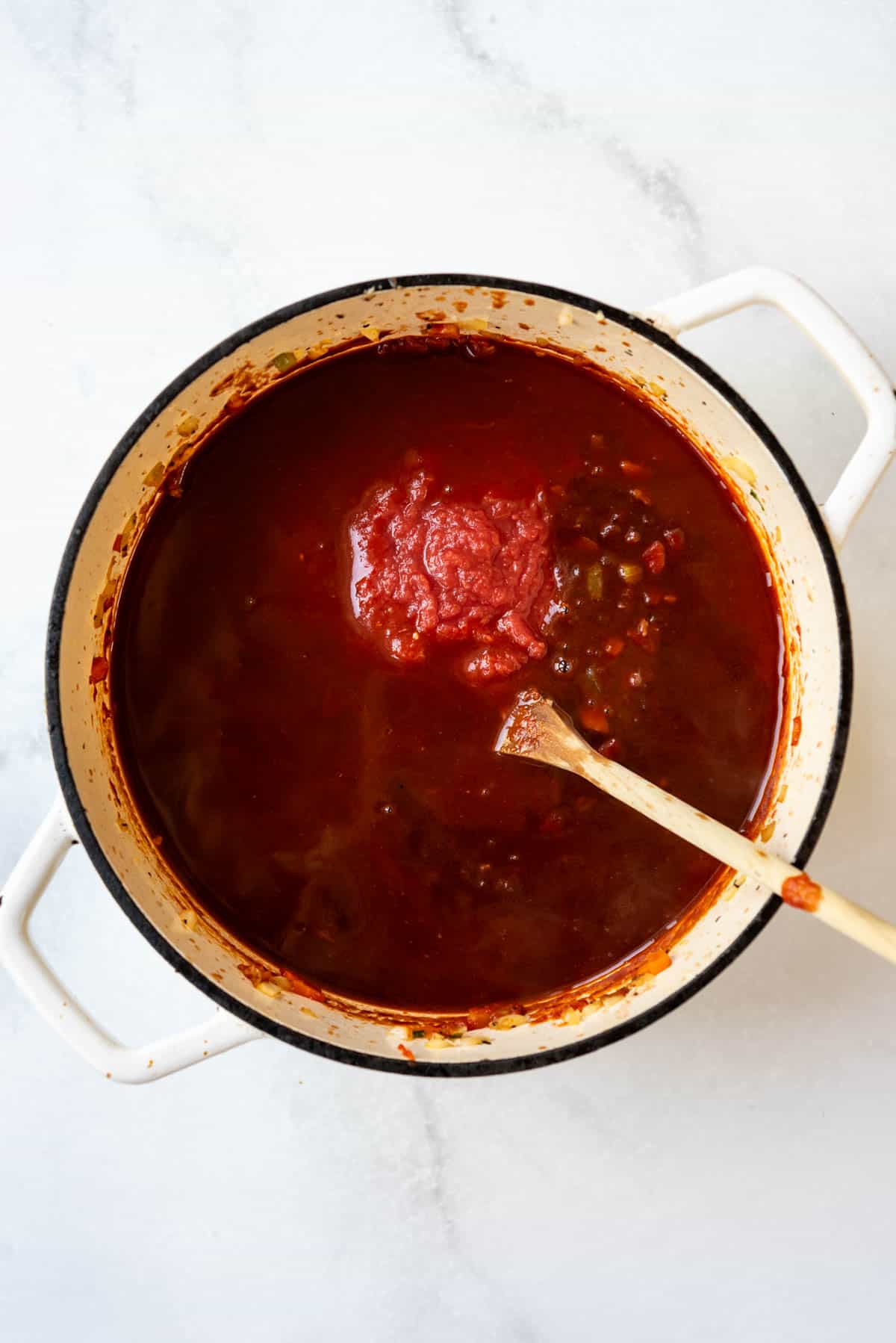 Adding broth to a pot of sauteed vegetables for making beef ragu.