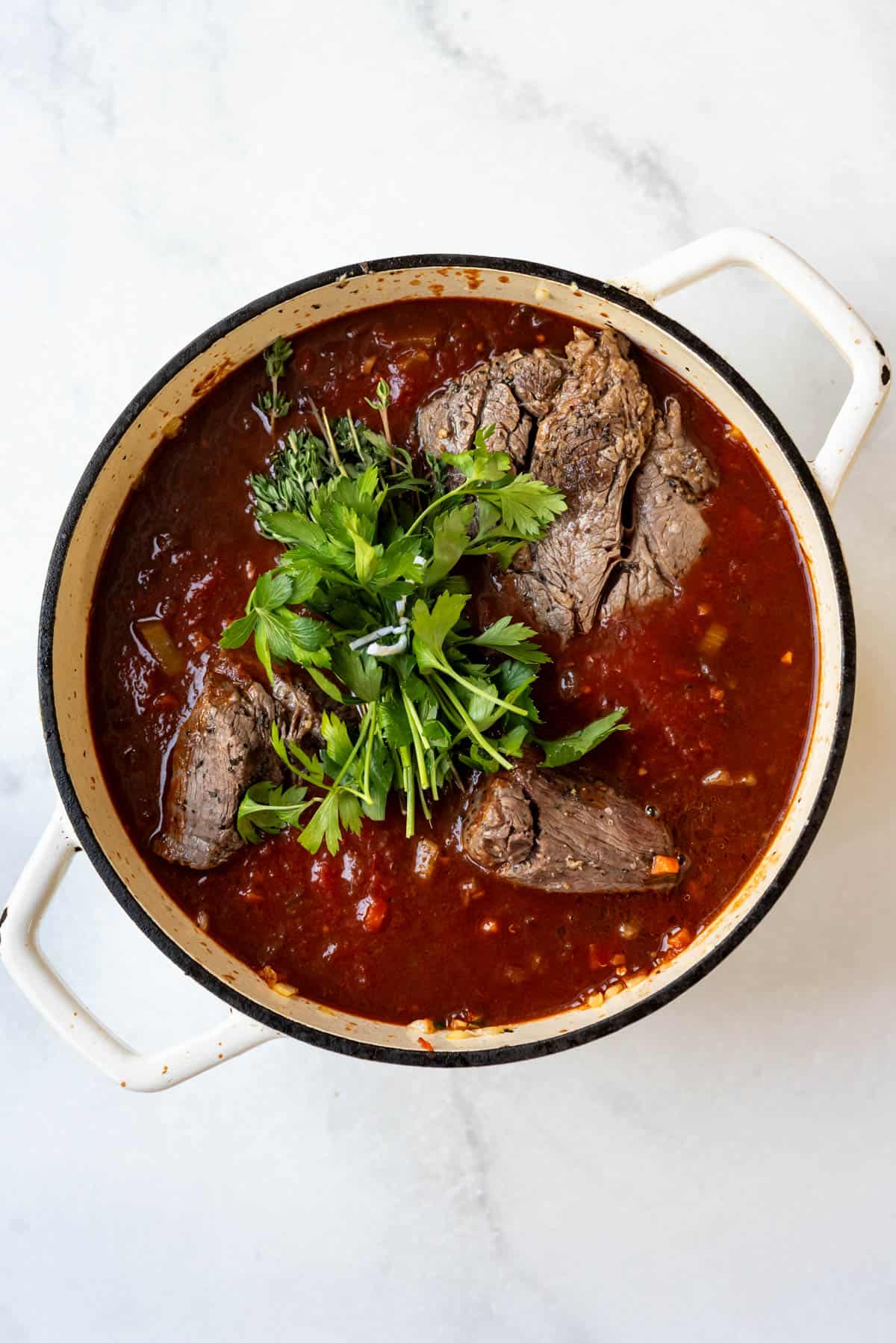 Adding parsley and seared beef to a pot of vegetables and liquid to make beef ragu.