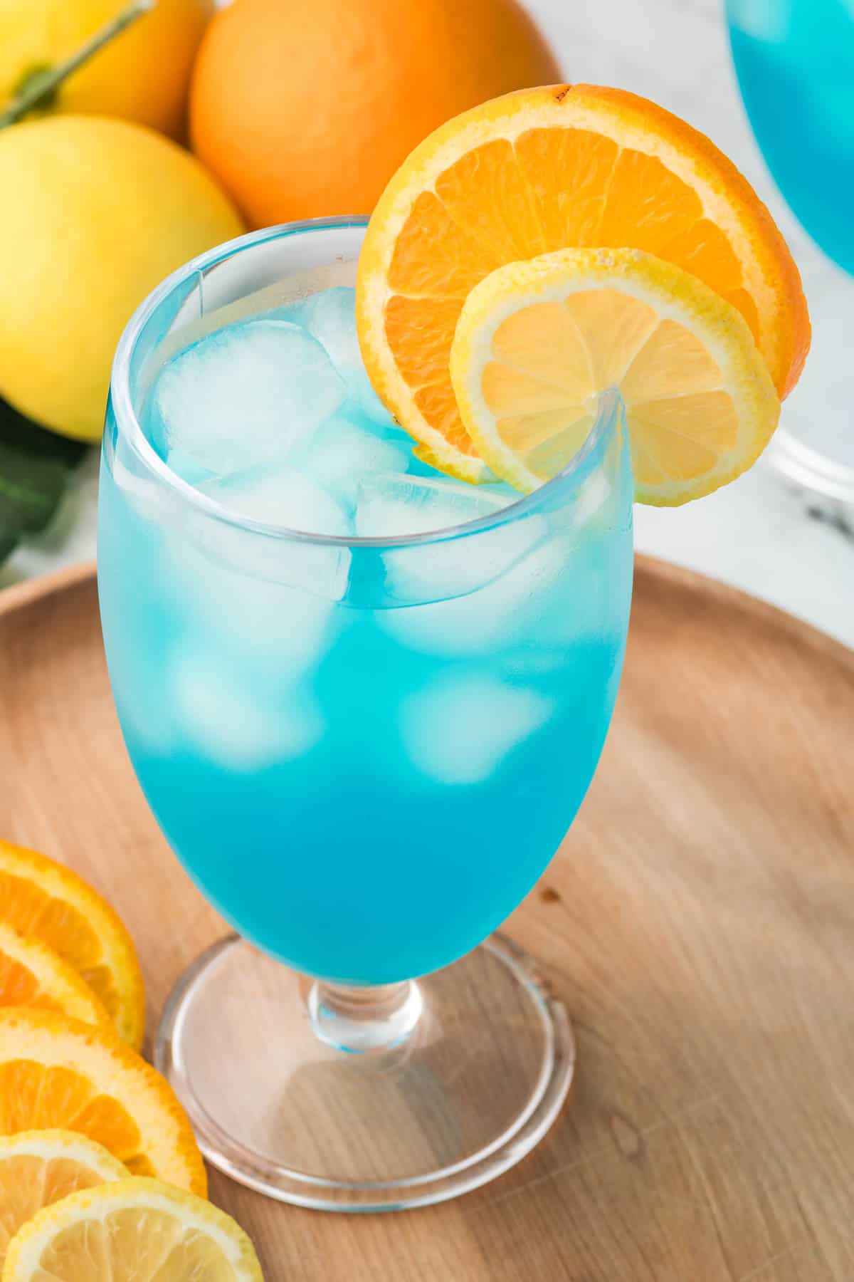 An overhead image of a blue lagoon mocktail in a glass with sliced oranges and lemons around it.